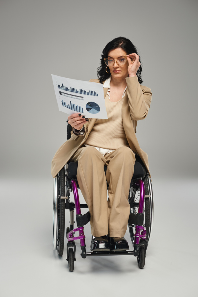atractiva mujer morena con discapacidad con gafas trabajando en gráficos mientras está en silla de ruedas - Foto, imagen