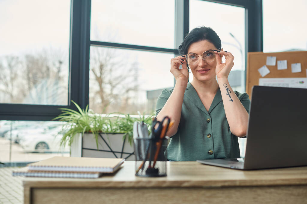beautiful disabled woman in casual attire with tattoo and glasses looking away while in office - Photo, Image