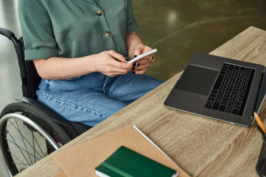 Ausgeschnittene Ansicht einer behinderten Frau in Freizeitkleidung, die im Rollstuhl sitzt und an ihrem Laptop arbeitet - Foto, Bild