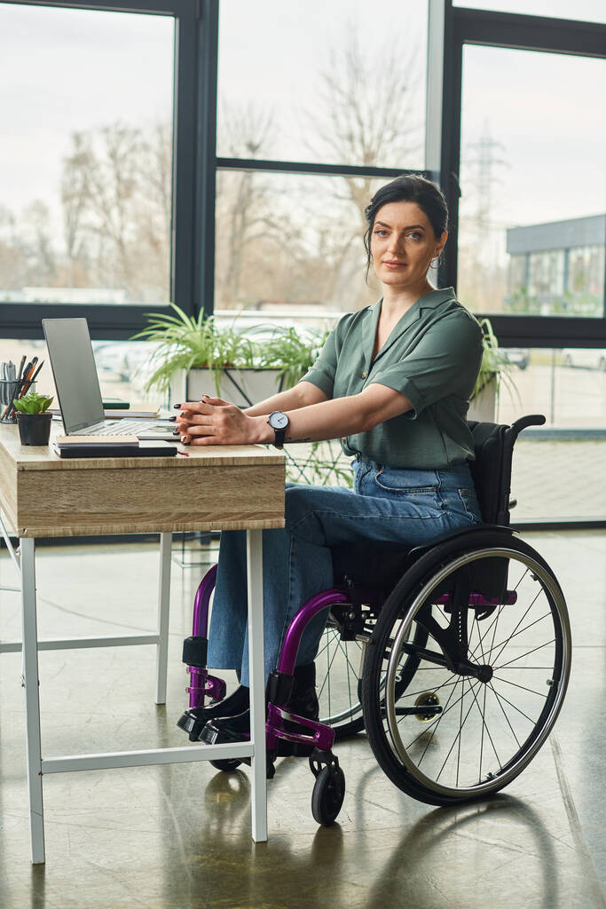 χαρούμενη επιχειρηματίας με αναπηρία με περιστασιακή ενδυμασία σε αναπηρική καρέκλα κοιτάζοντας την κάμερα, ενώ εργάζονται σκληρά - Φωτογραφία, εικόνα
