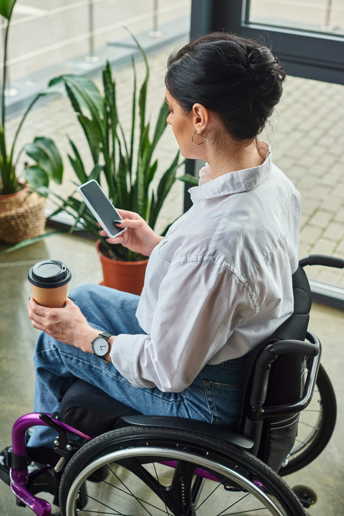 コーヒーと電話を保持するエレガントな服装で車椅子に障害のある魅力的な専用女性 - 写真・画像