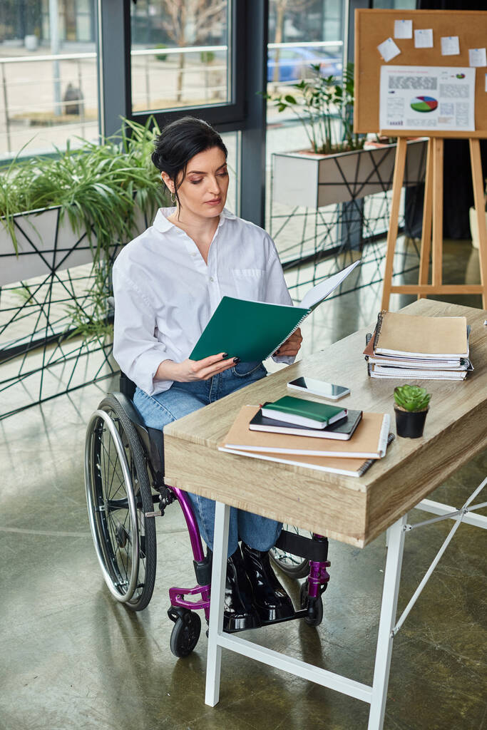 omistautunut liikuntarajoitteinen liikenainen pyörätuolissa tutustumassa toimistossaan oleviin papereihin - Valokuva, kuva