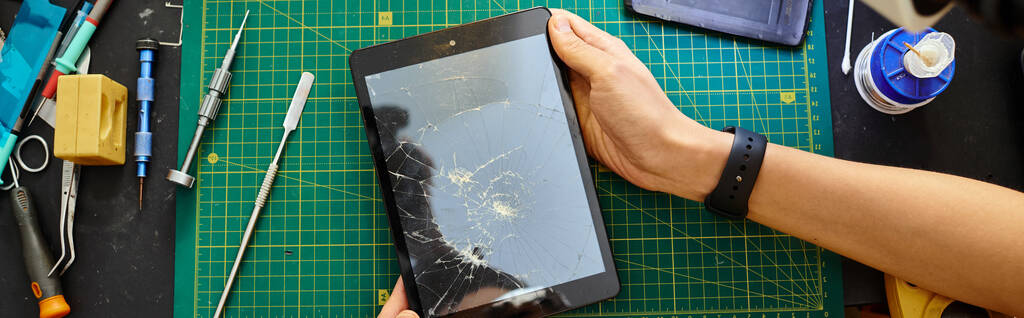 częściowy widok doświadczonego technika trzymającego tablet cyfrowy z zepsutym ekranem w warsztacie, baner - Zdjęcie, obraz