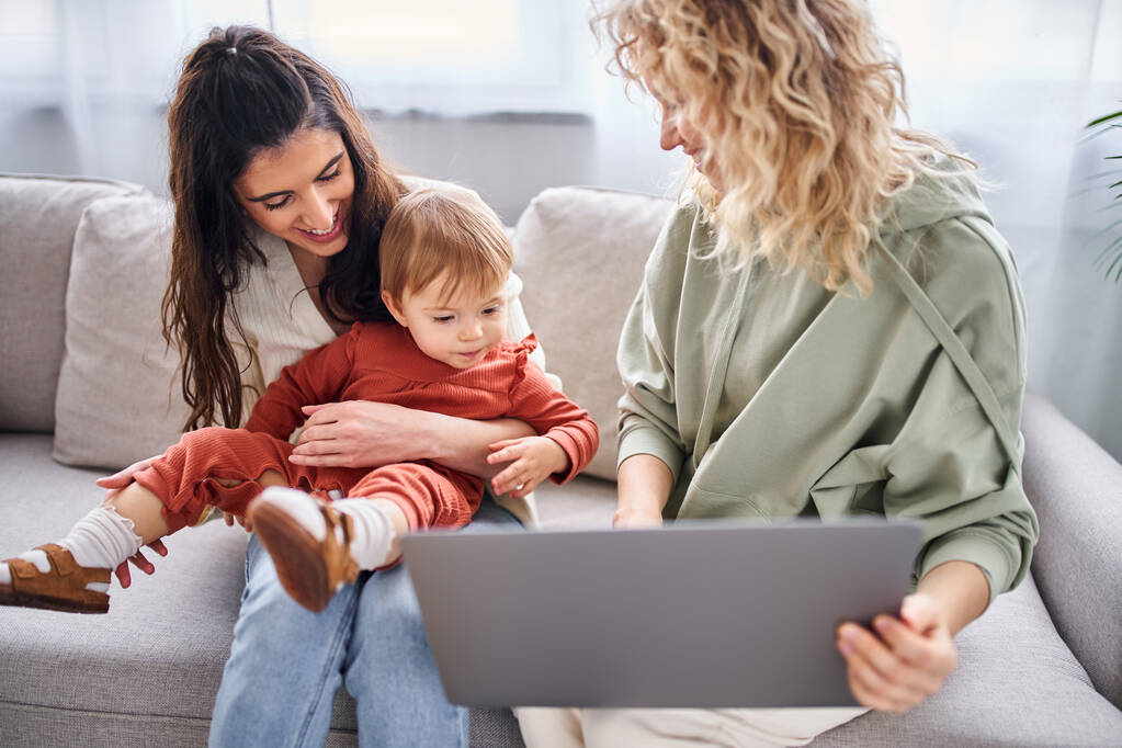 allegra coppia lesbica amorevole seduta sul divano con la loro bambina guardando laptop, famiglia - Foto, immagini