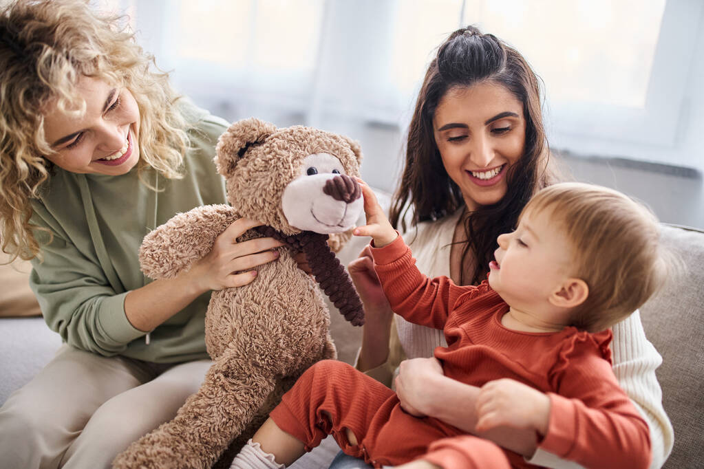 όμορφο ευτυχισμένο ζευγάρι λεσβιών με την κόρη τους νήπιο και αρκουδάκι στον καναπέ, οικογενειακή ιδέα - Φωτογραφία, εικόνα