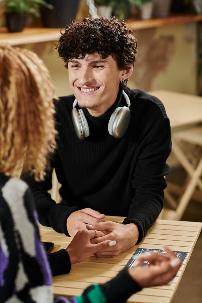 curly young man with wireless headphones holding hand of african american girl in vegan cafe - Photo, Image