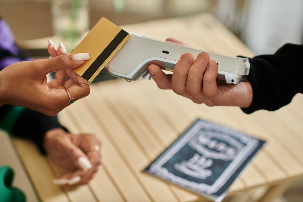 женщина-клиент держит кредитную карту рядом с кард-ридером, обрезанная рука на женщине, платящей в веганском кафе - Фото, изображение