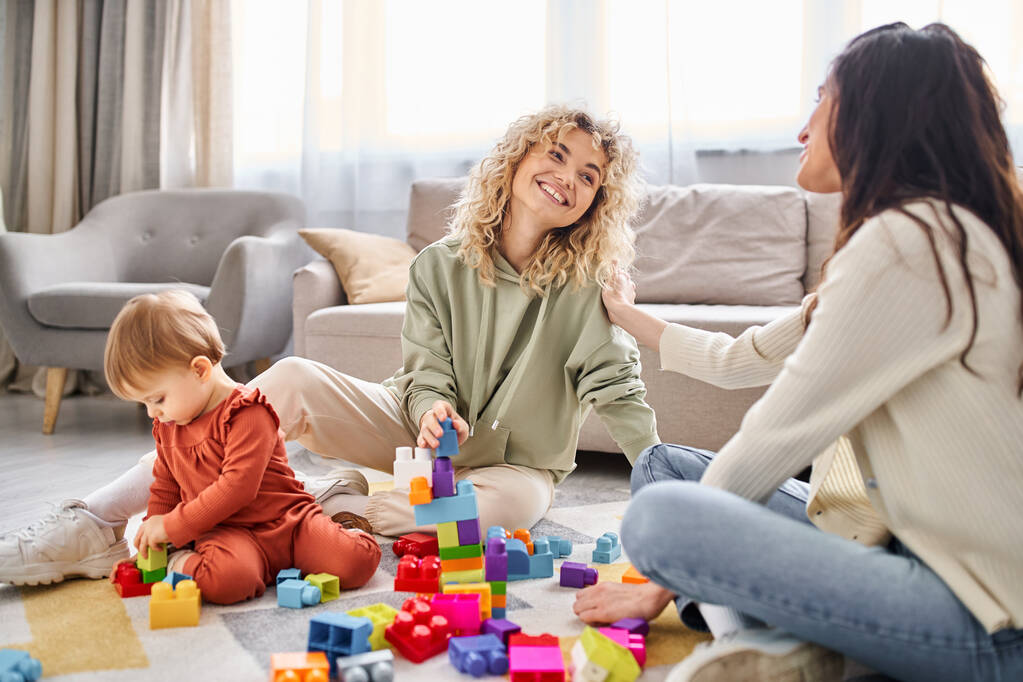 alegre amante lgbt pareja jugando con su bebé niña con juguetes en el suelo en casa, concepto de familia - Foto, Imagen