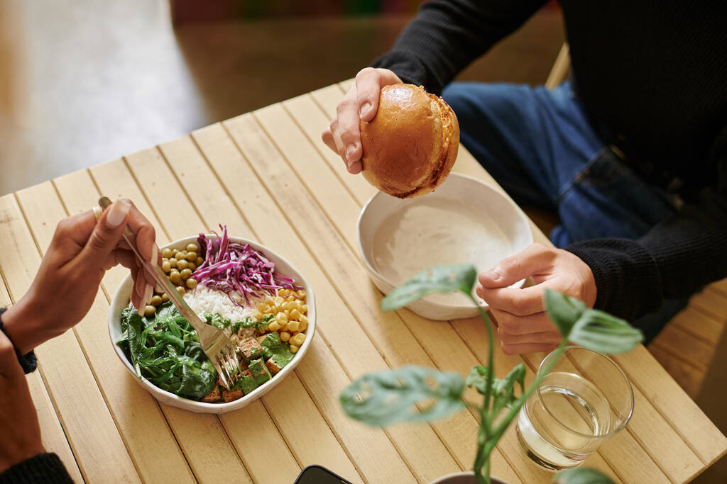 top view of young and diverse couple enjoying vegan meal in cafe, burger with tofu and salad bowl - Photo, Image
