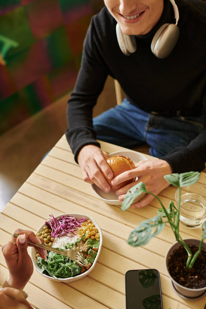 Blick von oben auf junge Paare, die veganes Essen im Café, Burger mit Tofu und Salatschüssel genießen - Foto, Bild