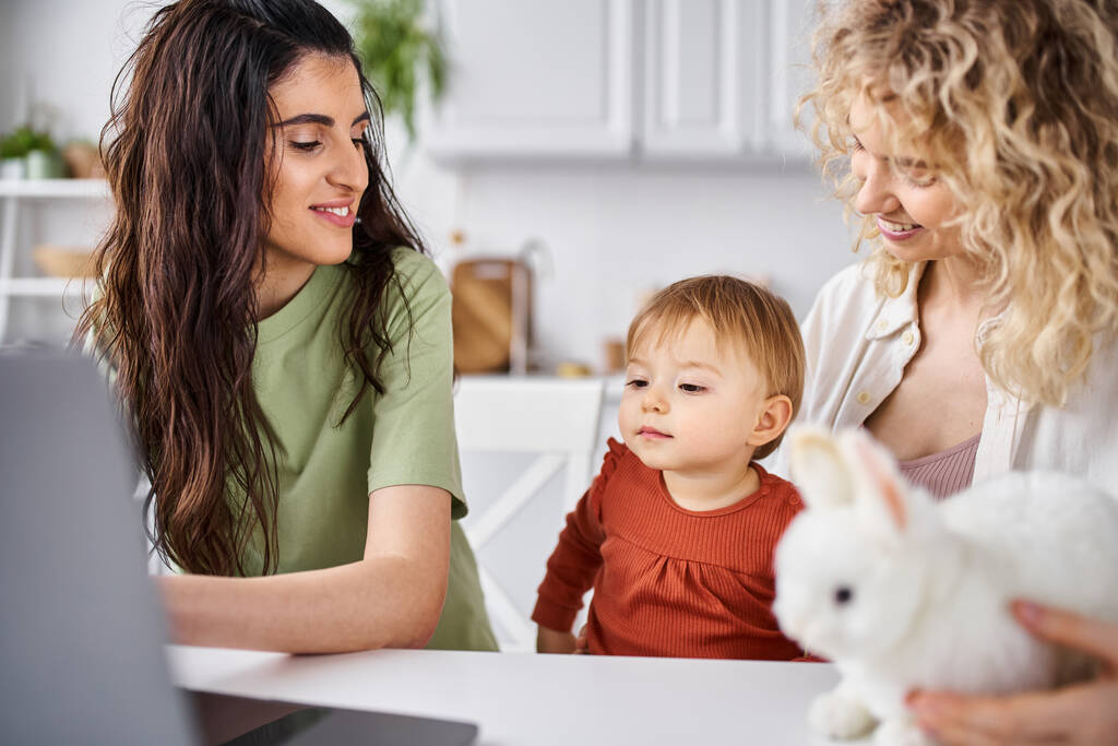 attractive lesbian couple in homewear watching movies with their baby girl on laptop, family concept - Photo, Image