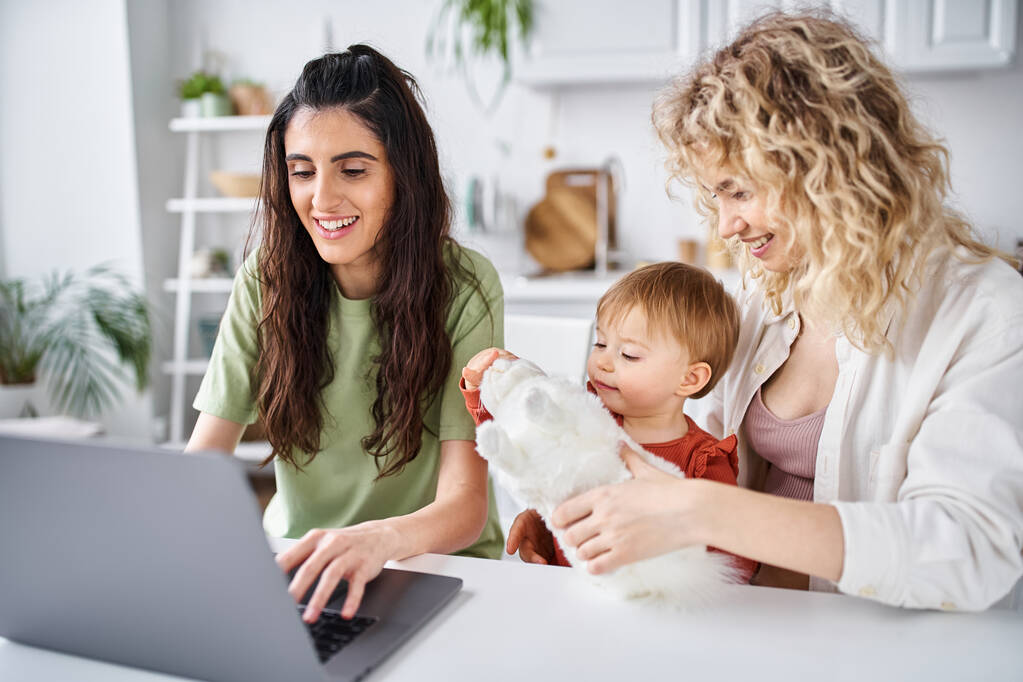 nurturing lesbian couple in homewear watching movies with their baby girl on laptop, family concept - Photo, Image
