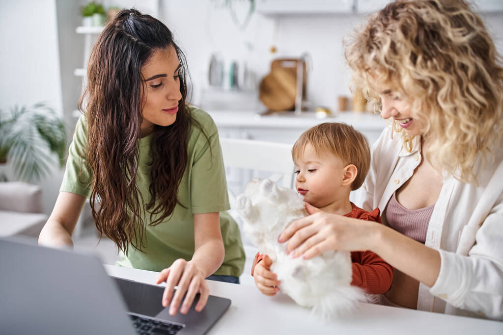 pretty lesbian couple in homewear watching movies with their baby girl on laptop, family concept - Photo, Image