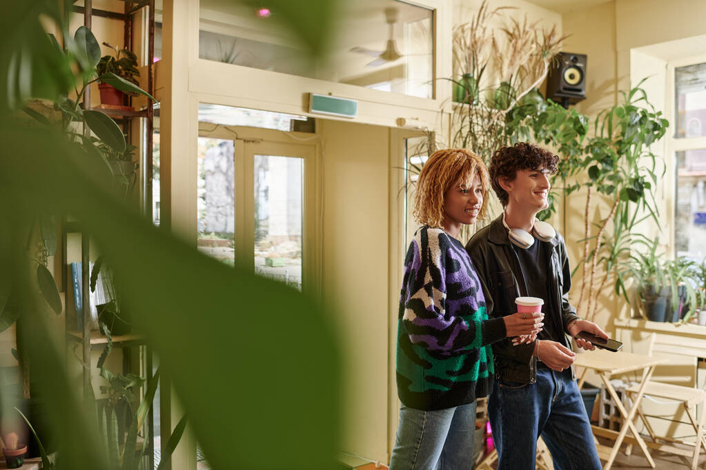 radosna i zróżnicowana para w stroju casual spacery z cappuccino na bazie roślin w wegańskiej kawiarni - Zdjęcie, obraz