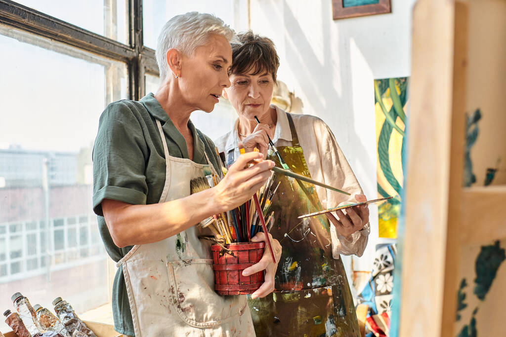 getalenteerde volwassen vrouwelijke kunstenaars kiezen penselen tijdens masterclass in ambachtelijke workshop - Foto, afbeelding