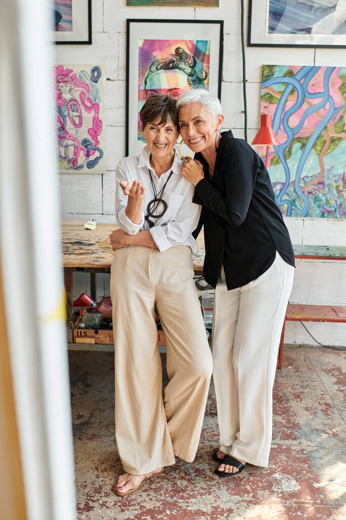 Heyecanlı orta yaşlı kadın sanatçı modern sanat atölyesinde lezbiyen ortağının elini gösteriyor. - Fotoğraf, Görsel