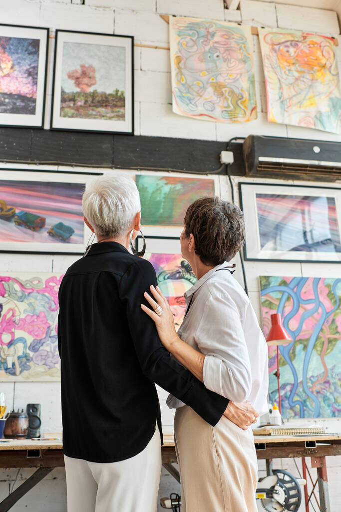 achteraanzicht van lesbisch paar kunstenaars op zoek naar creatieve levendige schilderijen in moderne kunst workshop - Foto, afbeelding