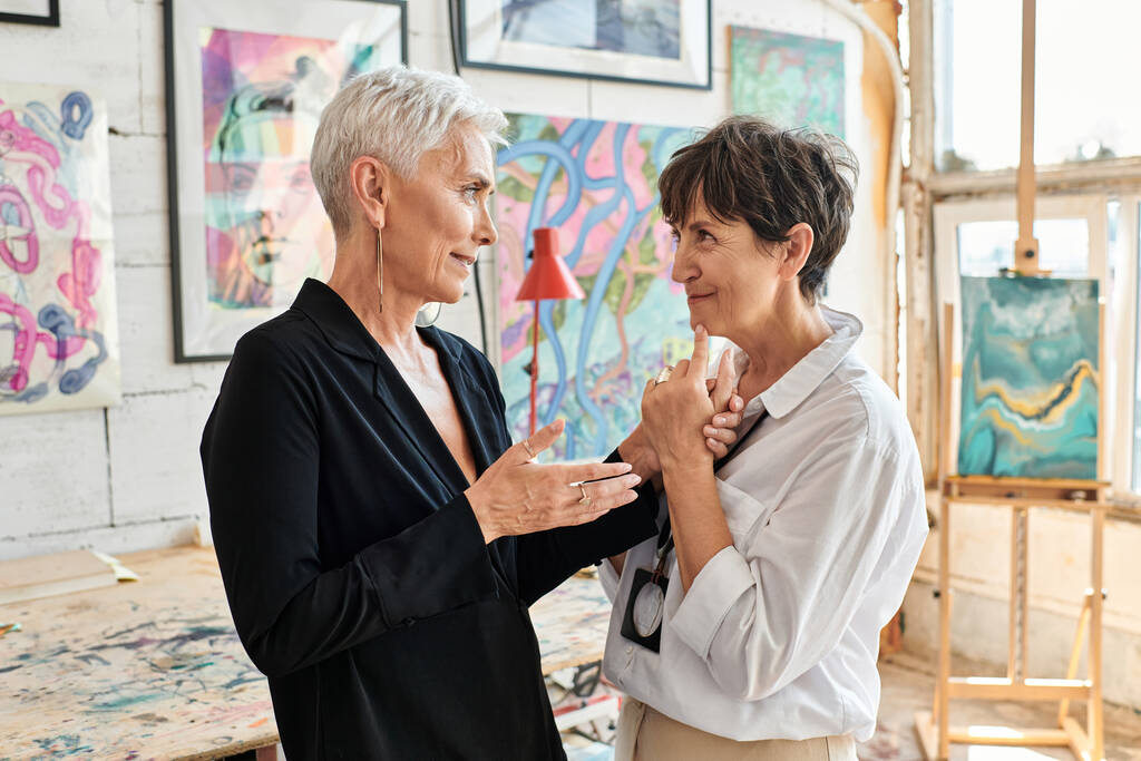 vista lateral de feliz y elegante pareja de artistas lesbianas hablando en el taller de arte moderno, trabajo en equipo - Foto, imagen
