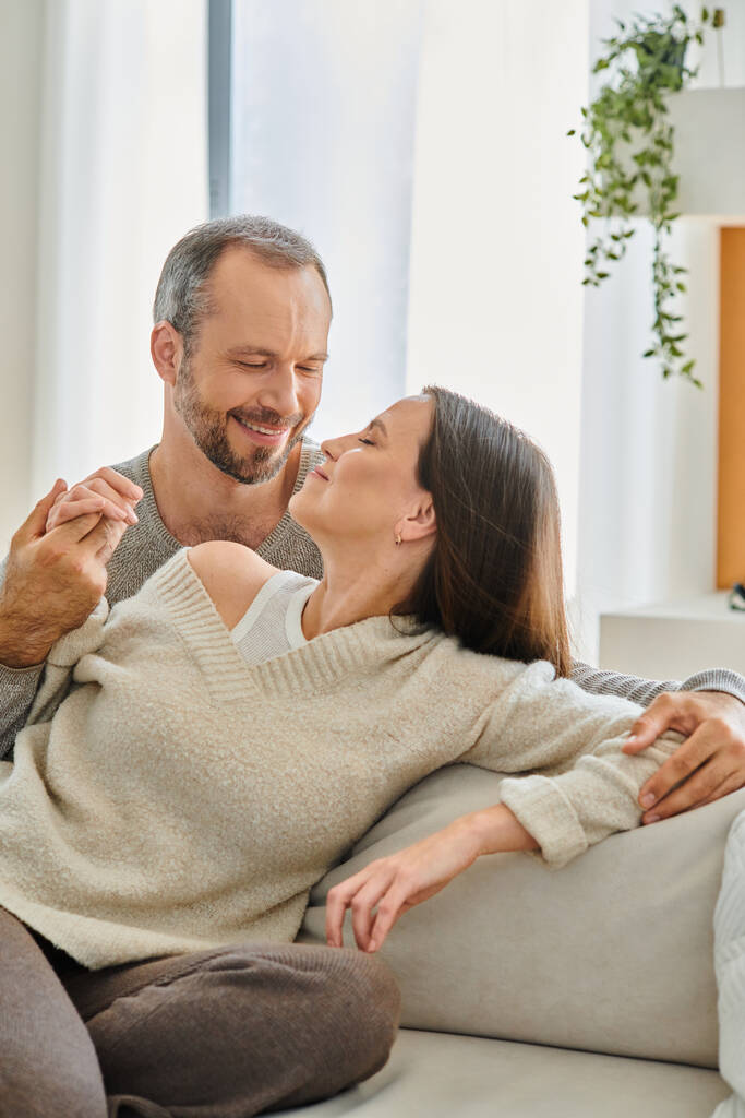 pleased child-free couple holding hands while sitting on couch in cozy living room, relax and fun - Photo, Image