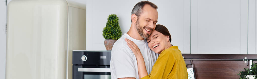 веселая пара без детей обнимается и улыбается с закрытыми глазами на кухне, горизонтальное знамя - Фото, изображение