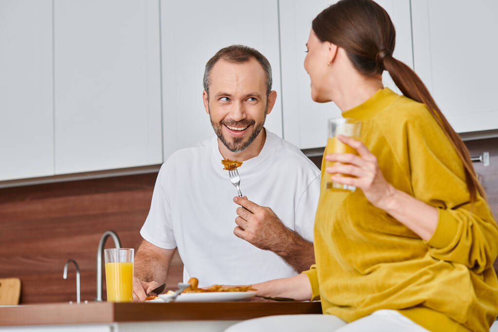 vreugdevolle man met heerlijk ontbijt bij vrouw met sinaasappelsap in keuken, kindvrije levensstijl - Foto, afbeelding