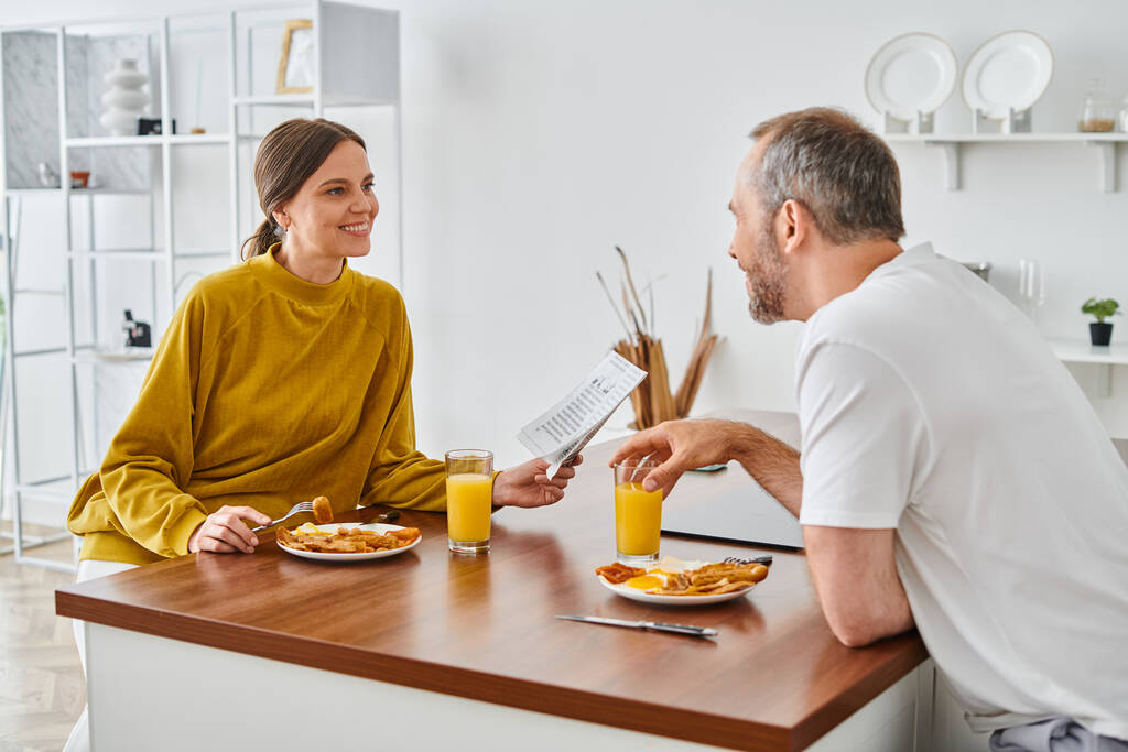 веселая женщина читает газету во время завтрака с мужем на кухне, образ жизни без детей - Фото, изображение