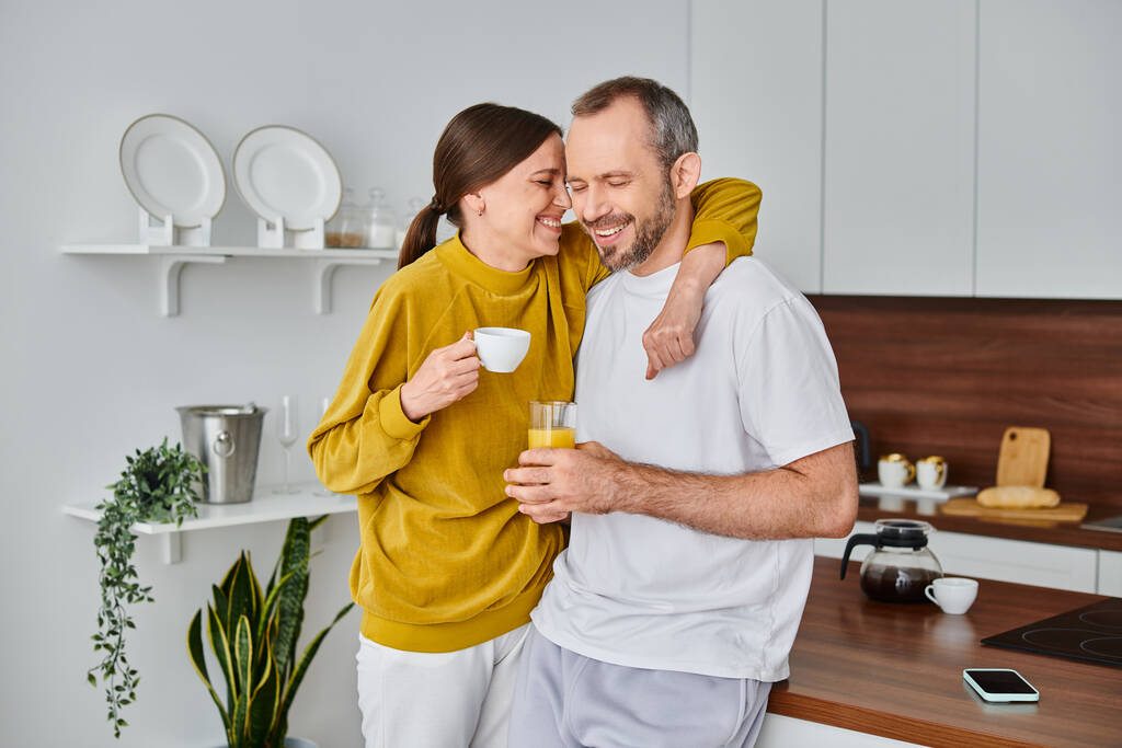 örömteli gyermekmentes pár kávéval és friss narancslével mosolyogva csukott szemmel a konyhában - Fotó, kép