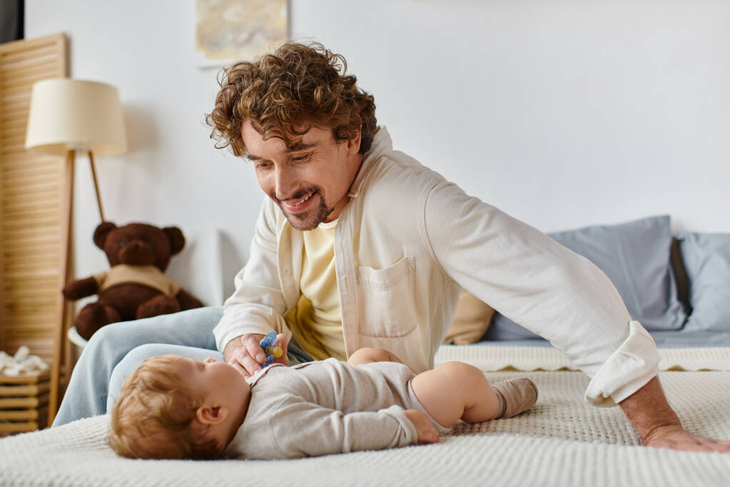 pai solteiro alegre dando chupeta para seu filho bebê bebê na cama, paternidade e amor - Foto, Imagem