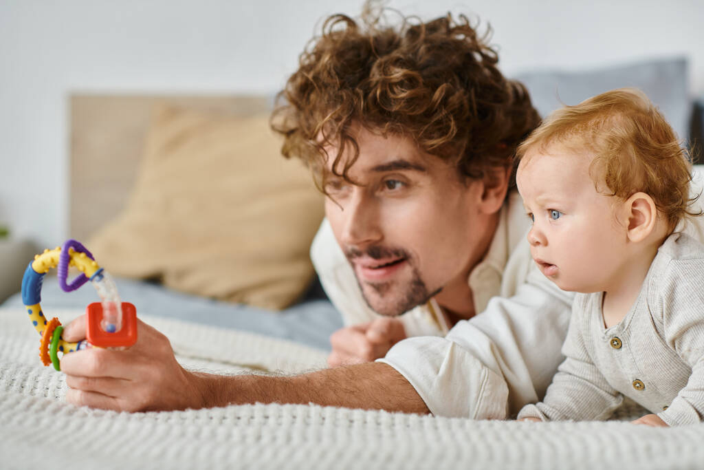 père célibataire et bébé garçon captivé par hochet coloré dans la chambre à coucher, lien entre parent et enfant - Photo, image