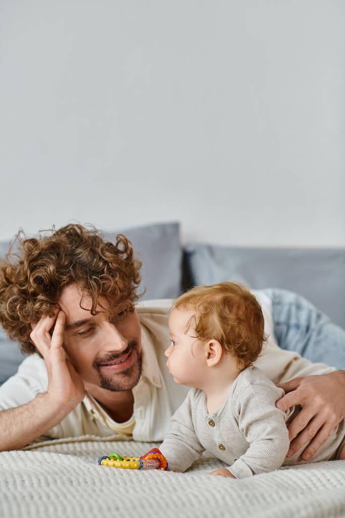 homme regardant son bébé garçon près hochet coloré dans la chambre à coucher, lien entre père et fils - Photo, image