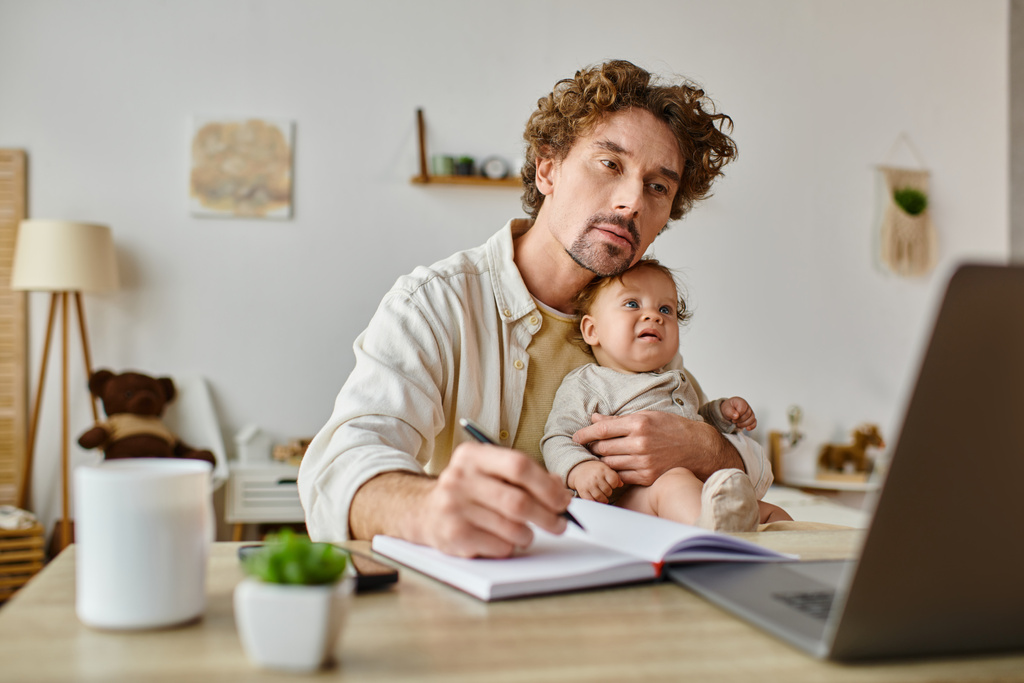 drukke alleenstaande vader houdt zijn zoontje in handen terwijl hij thuis werkt, werk-privébalans - Foto, afbeelding