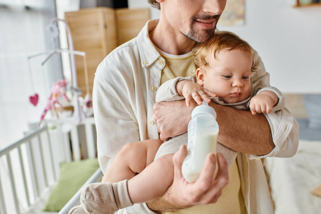 обрезанный отец внимательно кормит своего младенца молоком в детской бутылочке, отцовством и заботой - Фото, изображение