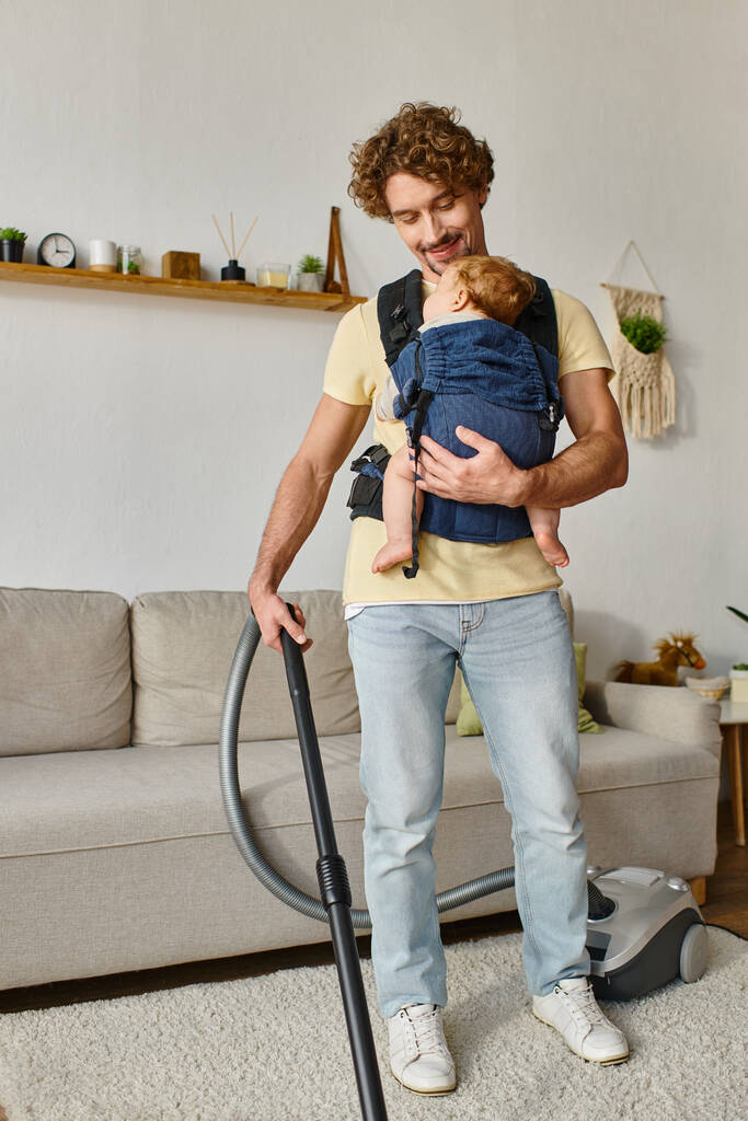 glücklicher Vater mit Säugling im Tragetuch saugenden Wohnzimmer, Sauberkeit und Hausarbeit - Foto, Bild