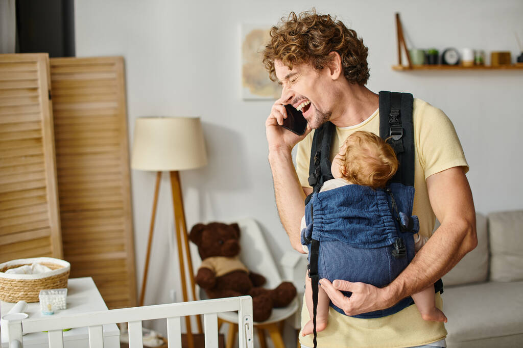 gelukkig vader praten op smartphone met baby slapen in drager, balans tussen leven en werk - Foto, afbeelding