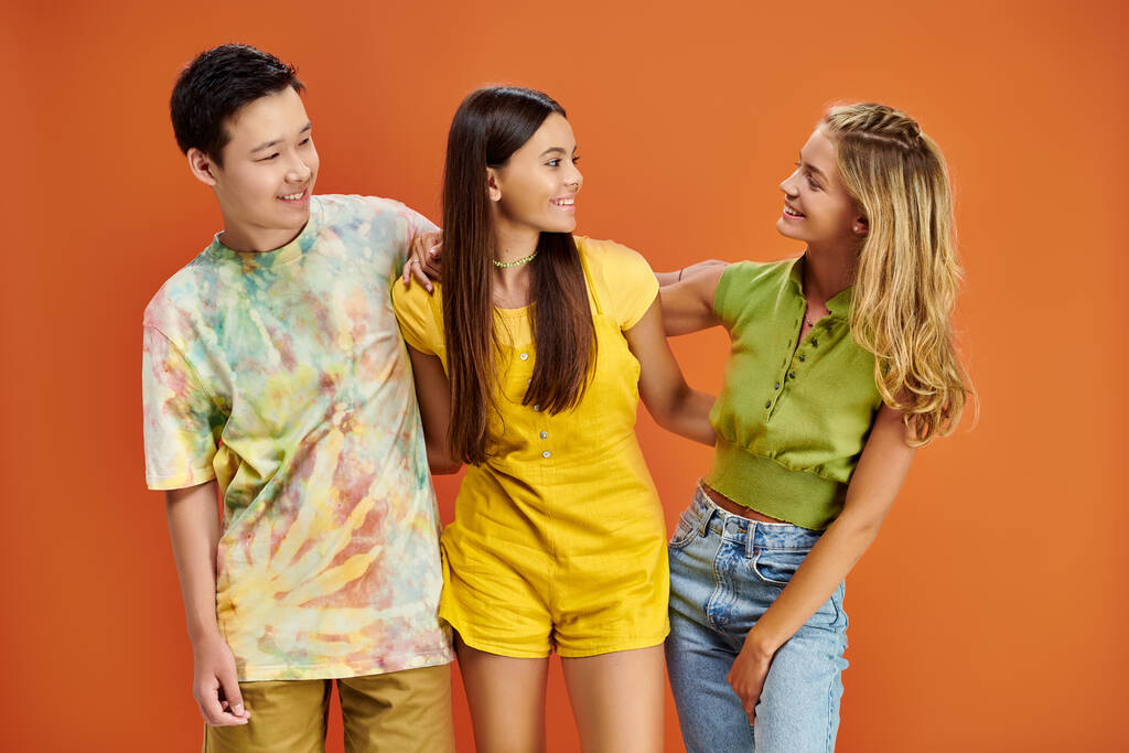 tres adolescentes alegres diversos en trajes casuales vibrantes mirándose, día de la amistad - Foto, imagen