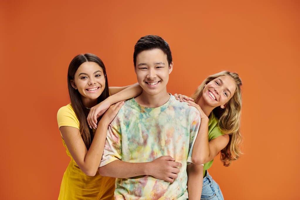 vrolijke multiraciale tieners in levendige outfits glimlachen op camera op oranje achtergrond, vriendschap dag - Foto, afbeelding