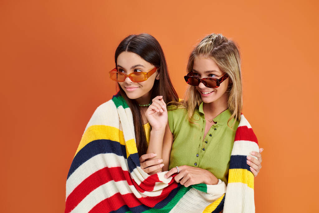 fröhliche entzückende Teenager mit Sonnenbrille, die mit einer Decke bedeckt ist und wegschaut, Freundschaftstag - Foto, Bild