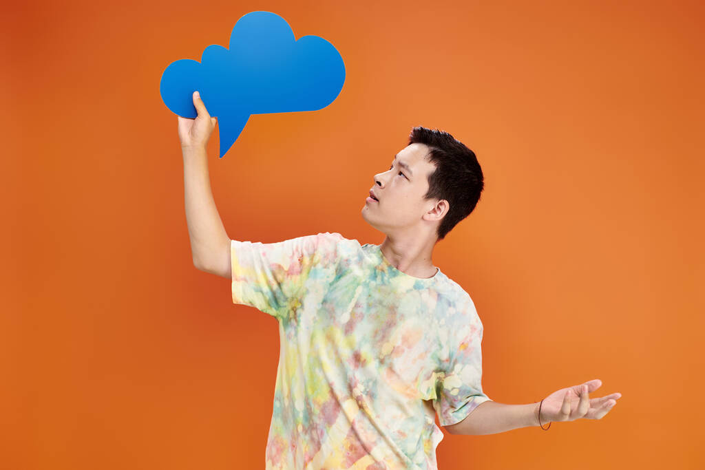 adolescent confus asiatique garçon dans tous les jours tenue regarder bleu pensée bulle sur orange toile de fond - Photo, image
