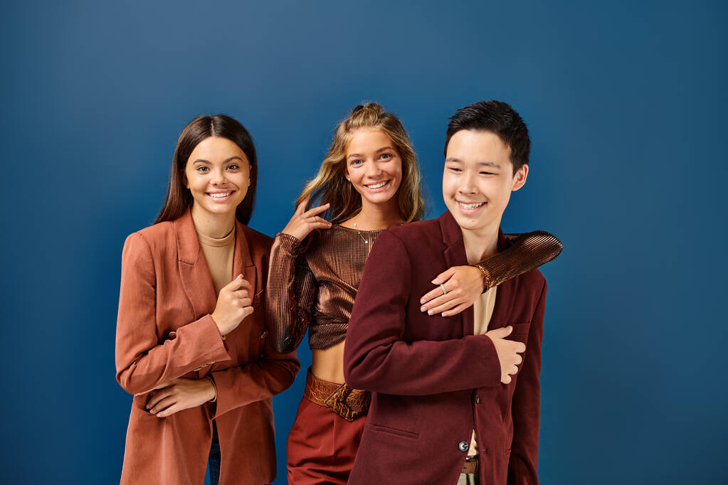 счастливые разнообразные подростки в стильных ярких нарядах позируют вместе на голубом фоне, день дружбы - Фото, изображение