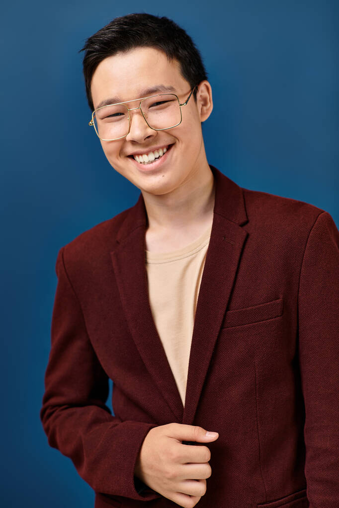 vrolijk elegant aziatisch tiener jongen in bril en stijlvolle kleding glimlachen op camera op blauwe achtergrond - Foto, afbeelding