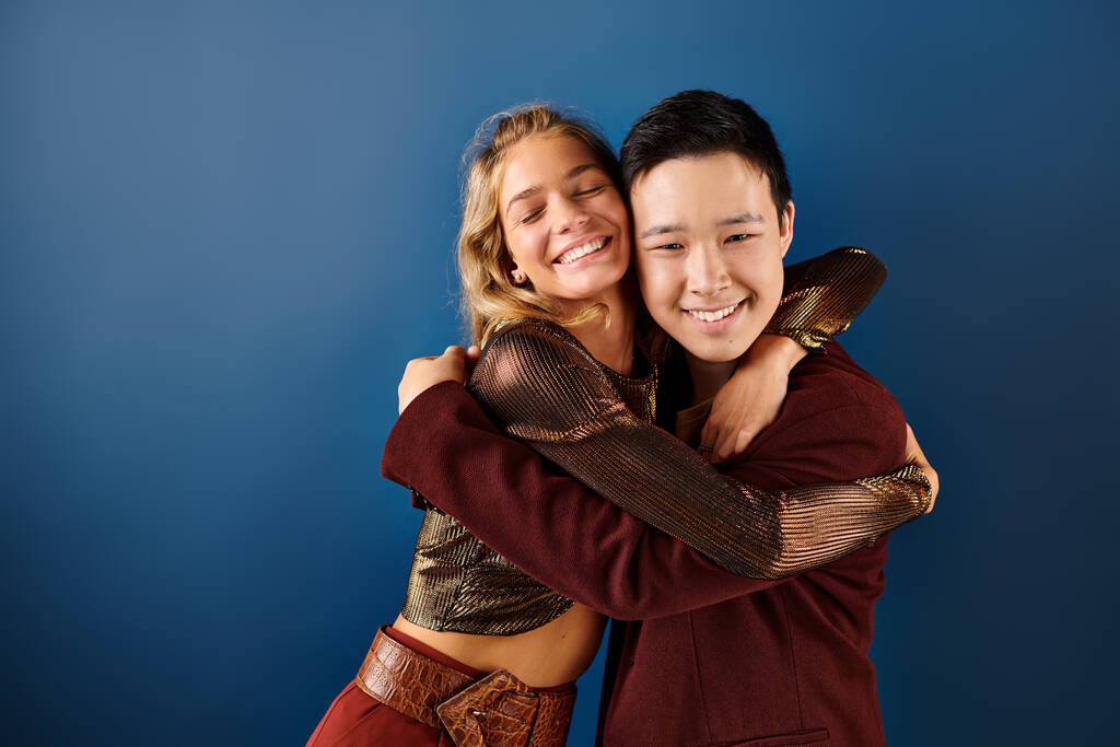 χαρούμενο έφηβο ξανθό κορίτσι και ασιατικό αγόρι αγκαλιάζει και χαμογελά στην κάμερα, ημέρα φιλίας - Φωτογραφία, εικόνα