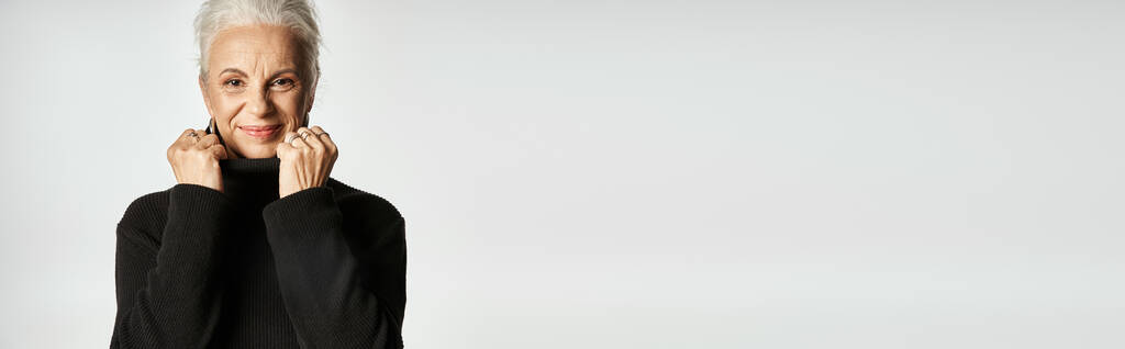 retrato de mulher de negócios de meia idade ajustando colarinho de camisola gola alta no fundo cinza - Foto, Imagem