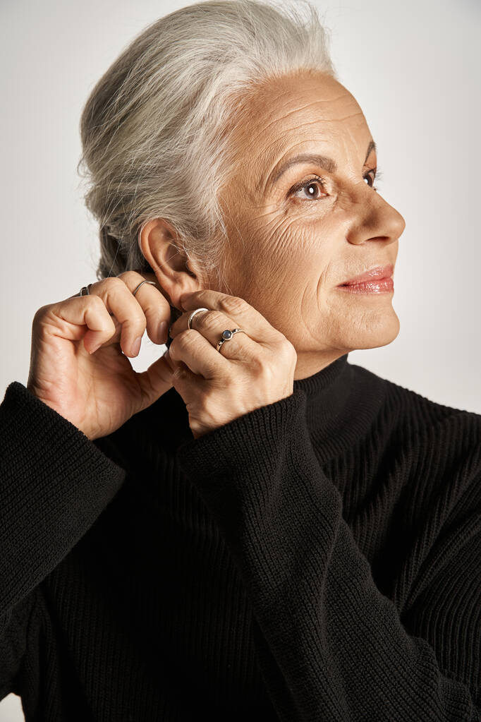 gelukkig middelbare leeftijd zakenvrouw in elegante kleding dragen hoepel oorbellen op grijze achtergrond - Foto, afbeelding