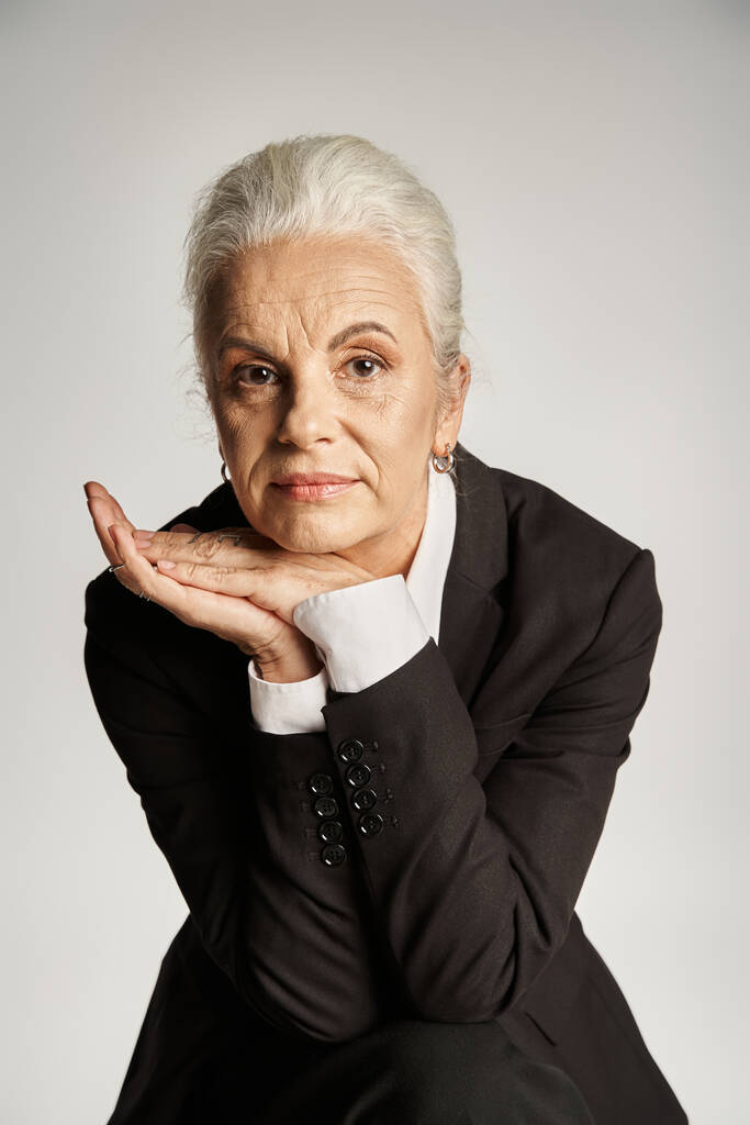 hermosa y gris mujer de mediana edad en traje elegante posando sobre fondo gris - Foto, imagen