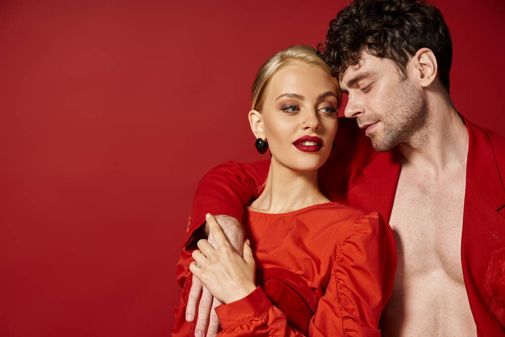 hombre guapo poniendo la mano alrededor del cuello de la hermosa mujer rubia con labios rojos en el telón de fondo vibrante - Foto, Imagen