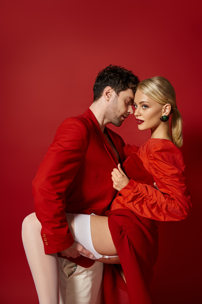 jóképű férfi emelés láb csábító szőke nő szexi fehér harisnya piros háttér - Fotó, kép