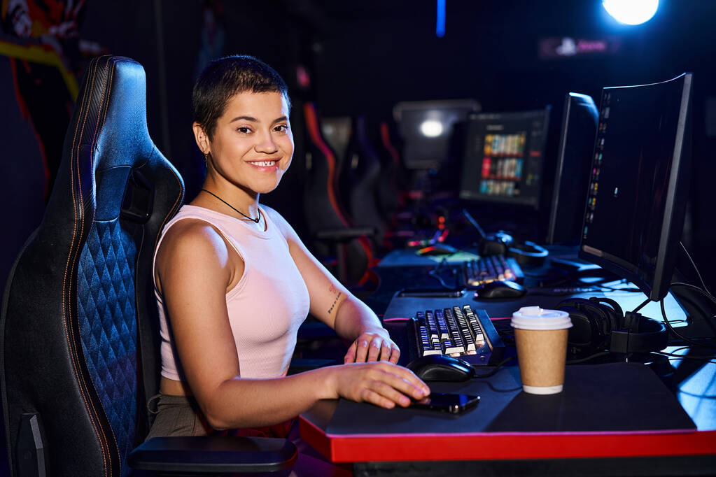 ευτυχισμένη γυναίκα ηλικίας zoomer κάθεται σε ένα γραφείο με οθόνη υπολογιστή και φλιτζάνι καφέ, Cybersport παιχνίδια - Φωτογραφία, εικόνα