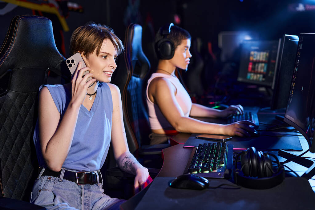 жінка сидить за комп'ютерним столом, розмовляючи по телефону біля друга, граючи в комп'ютерній грі в клубі - Фото, зображення
