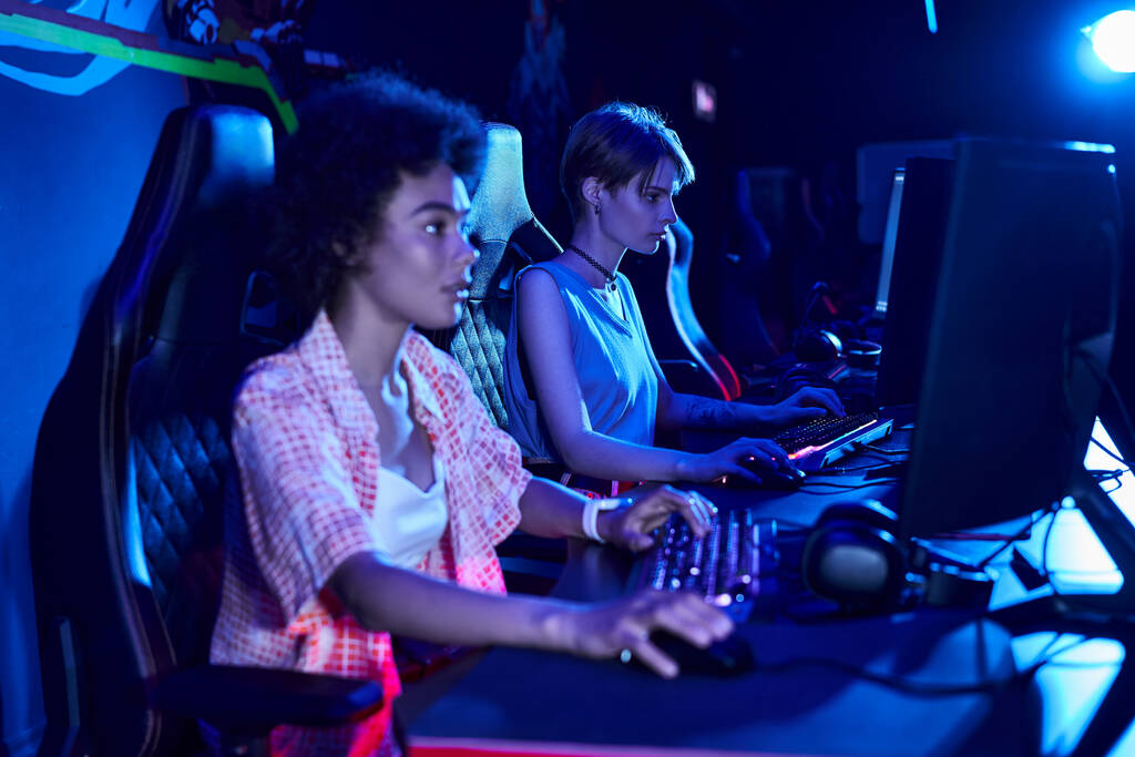 Genç Afro-Amerikan kadınlarının yoğun bir şekilde mavi ışıklı, siber spor konseptinde oynamasına odaklan. - Fotoğraf, Görsel