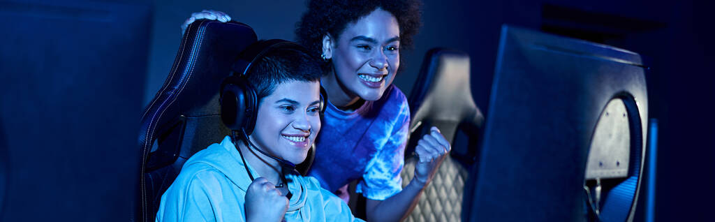 mujeres excitadas y jóvenes interracial ganar un juego en una sesión de juego de ciberdeporte, bandera horizontal - Foto, Imagen